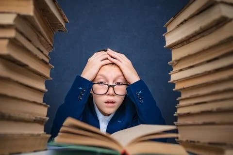 Smart boy in glasses sitting between two piles of books and read book Stock Photos