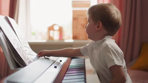 Smart boy turns music sheets sitting at electrical piano Stock Footage 244335022