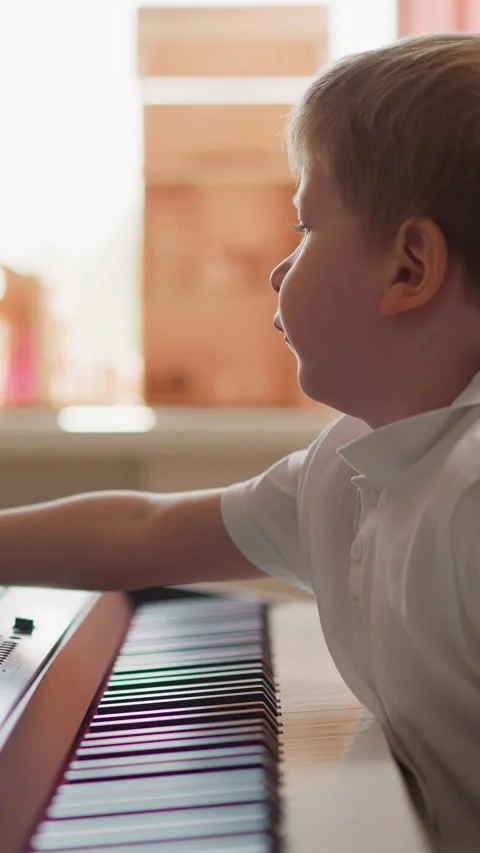 Smart boy turns music sheets sitting at electrical piano Stock Footage 307461288