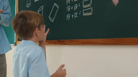 Smart boy writing answer at blackboard while teacher looking at child. Pedagogy. Stock Footage 279593899