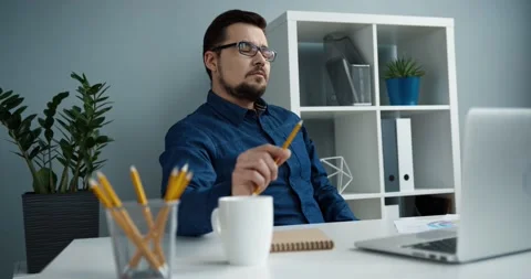 Smart Caucasian office worker with glasses sits at workplace and thinks about Stock Footage 147051916