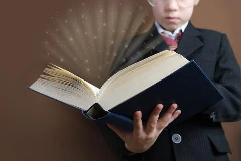 Smart child 7-8 years old, kid in black school suit stands and reads thick to Stock Photos