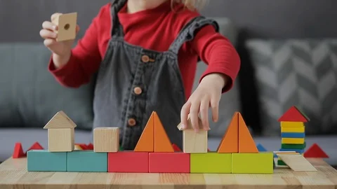 A smart child with glasses collects a multi-colored constructor at a table Stock Footage 128663912