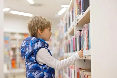 Smart child, school boy, educating himself in a library, borrowing books Stock Photos