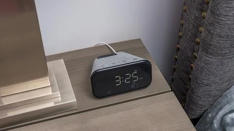 Smart clock with digital display showing time on a wooden bedside table next to 库存照片