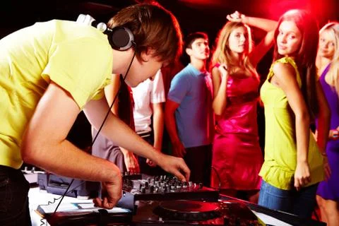 Smart deejay adjusting technics with dancing teens on background Stock Photos