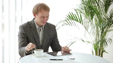 Smart dressed young man sitting at table using touchpad and smiling at camera Stock Footage 34278387