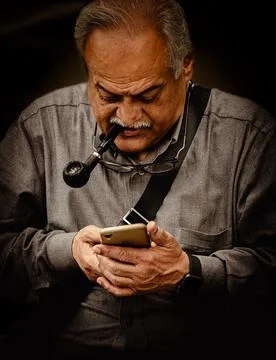Smart Elderly man sending a text message on the smartphone while smoking a pi Stock Photos