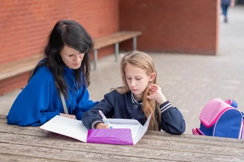 Smart girl solving math problems on her own while her mother sits nearby at a Stock Photos