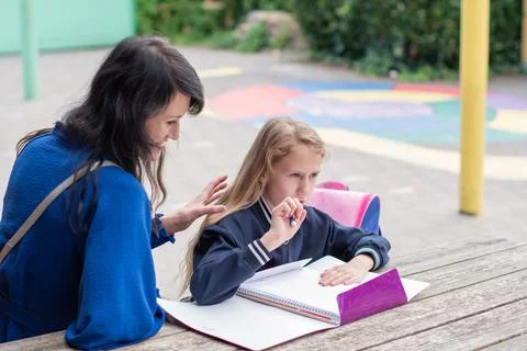 Smart girl solving math problems on her own while her mother sits nearby at a Foto stock