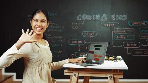Smart girl waving to camera while programing code at blackboard. Edification. Stockfoto's