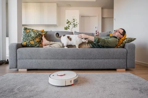 Smart home concept. man resting on the sofa while robot vacuum cleaner cleaning Stock Photos