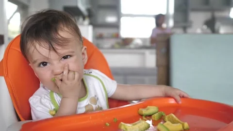 A smart kid eats avocado fruits with pleasure while sitting at a feeding table Stock Footage 184734171