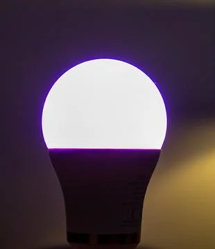 Smart LED Light Bulb Glowing Purple and White in Dark Interior	 Stock Photos