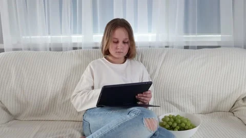 Smart little girl using tablet computer while sitting on couch Stock Footage 154693844