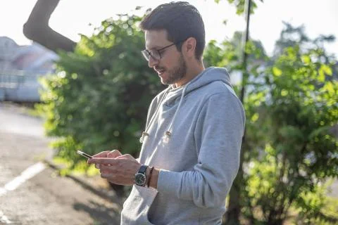 Smart looking man texting message on smartphone in park, back light Stock Photos