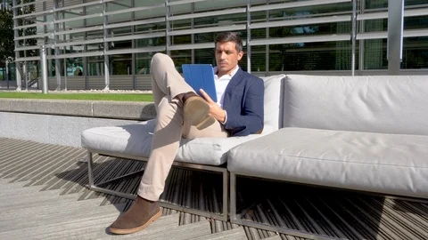 Smart man using tablet on outdoor sofa in trendy business park 4K Stock Footage 96057882