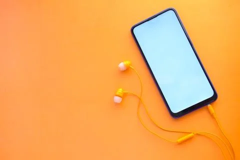 Smart phone with empty screen, earphone on orange background Stock Photos