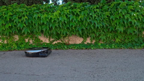 Smart robot vacuum cleaner running outdoors on grey asphalt driveway Video stock 335603988