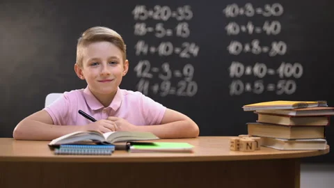 Smart schoolboy smiling to camera after solving task, exercises written behind Stock Footage 109586463