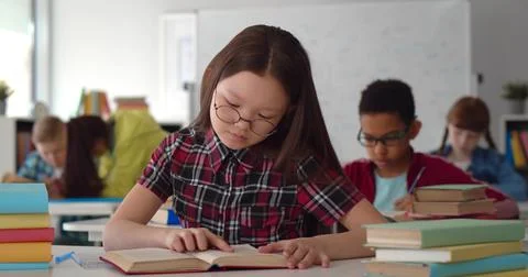Smart schoolgirl sitting in classroom and writing in textbook Stock Photos