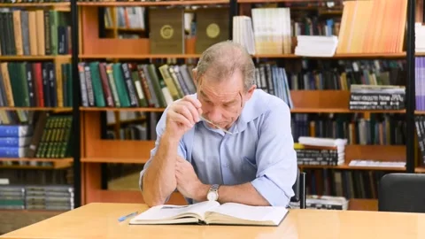 Smart senior man reading a book in the library Stock Footage 155034716