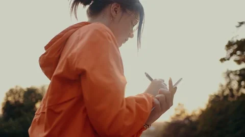 The smart student does her homework in the park. Dressed in a bright orange Stock Footage 160628297
