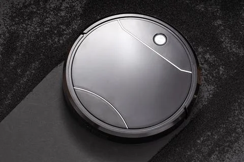 Smart vacuum cleaner working on a dark surface to remove dust and dirt Stock Photos