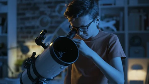 Smart young boy looking through a telescope at night Stock Footage 128499836