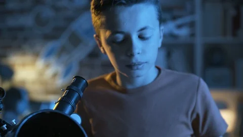 Smart young boy looking through a telescope at night Stock Footage 128500040