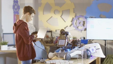 Smart Young Boy Programs Robot with a Laptop. He's Building Robot for Club 動画素材 75783283