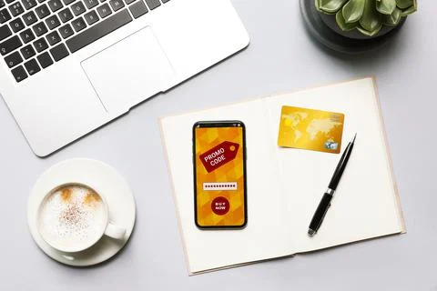 Smartphone with activated promo code, laptop and stationery on grey table, fl Stock Photos