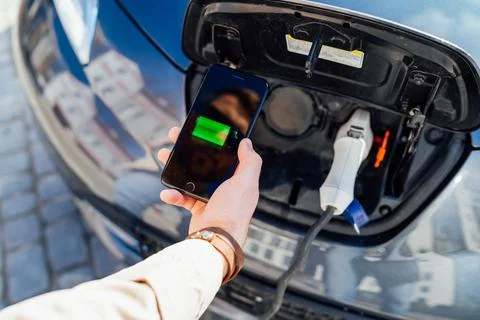 Smartphone app shows charging status of the electric car battery. Stock Photos