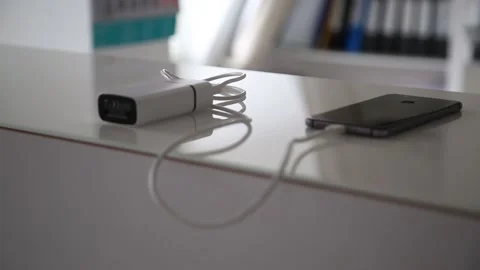 Smartphone is being charged via cable from charger on glass office table Stock Footage 141186311