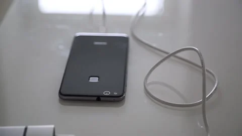 Smartphone is being charged via cable from charger on glass office table Stock Footage 141186322