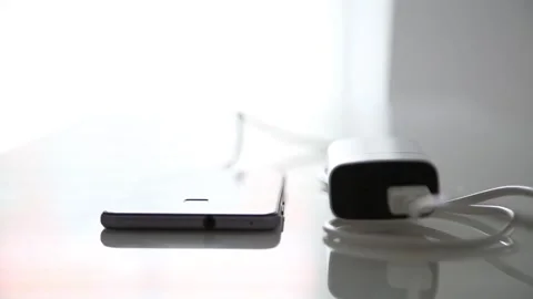 Smartphone is being charged via cable from charger on glass office table Stock Footage 141186330