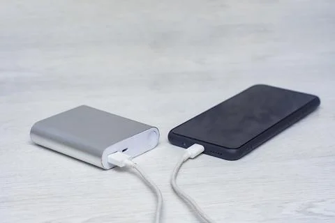 The smartphone is being charged using a portable charger on a wooden table. Stock Photos