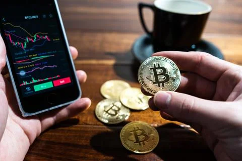 Smartphone with Bitcoin trading chart on the screen. Holding in hand a gold B Stock Photos