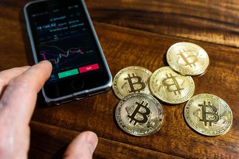 Smartphone with Bitcoin trading chart on the screen. Holding in hand a gold B Stock Photos