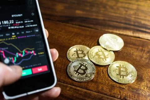 Smartphone with Bitcoin trading chart on the screen. Holding in hand a gold B Stock Photos