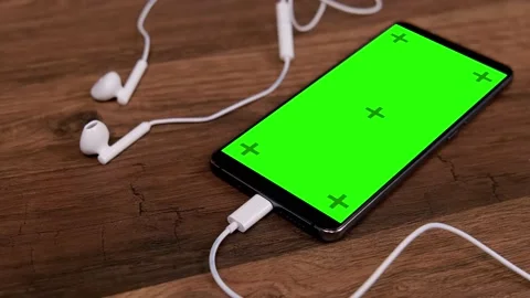 Smartphone with blank green screen and headphones on the table. Stock Footage 237474574