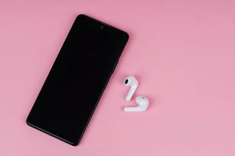 Smartphone with blank screen and white wireless earbuds on pink background... Stock Photos