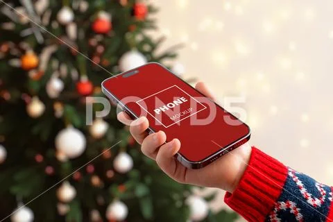 Smartphone with blank screen held near Christmas tree Modello PSD
