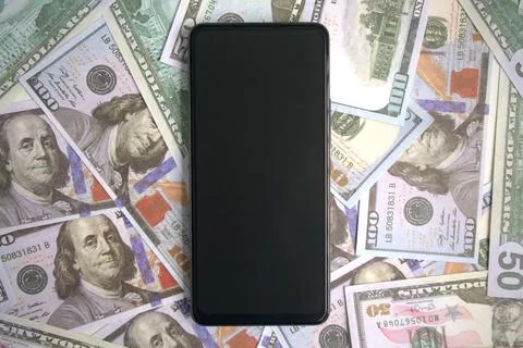 Smartphone with blank screen on top of a pile of dollar bills Stock Photos
