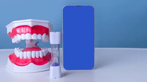 Smartphone with blue screen, denture model, and sand timer against blue backdrop Stock Photos