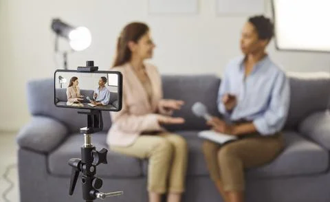Smartphone camera on tripod framing two women in a candid interview scene Stock Photos