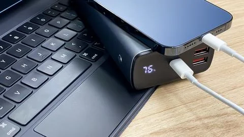 A smartphone is charging from an external battery next to a laptop. Fotos de archivo