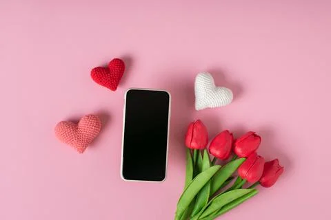 A smartphone with a clean screen with three knitted hearts and a bouquet of t Foto stock