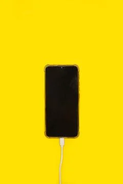 A smartphone connected to a charging cable on a yellow background Stock Photos