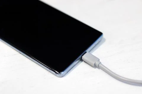 Smartphone connected to power. Wireless device linked to power source on wooden Stock Photos